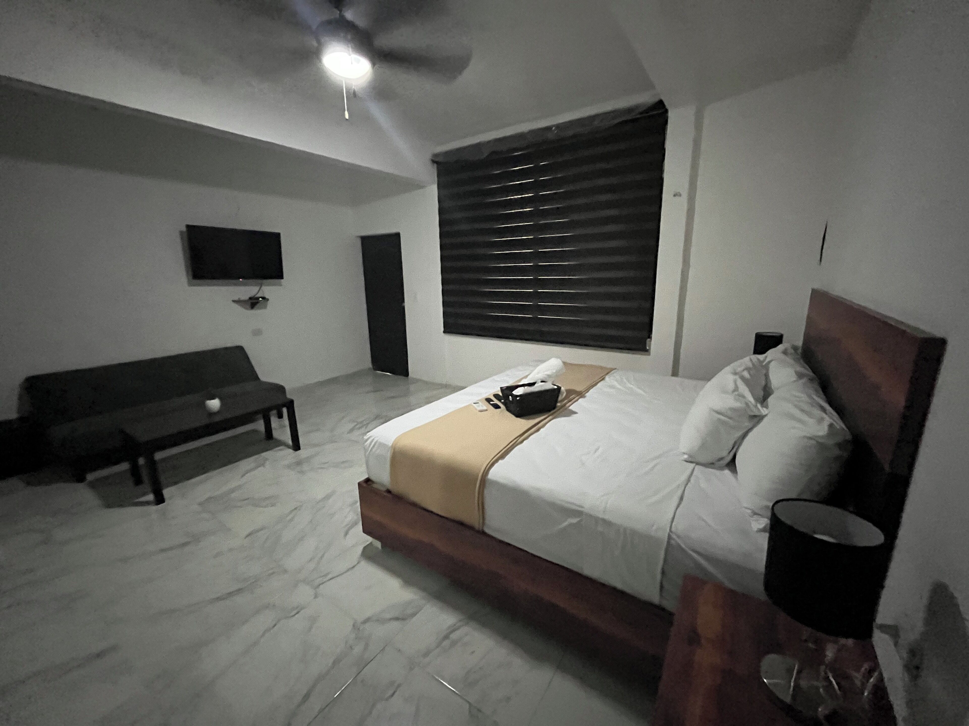A bedroom with a bed, a bench, a TV, and a ceiling fan.