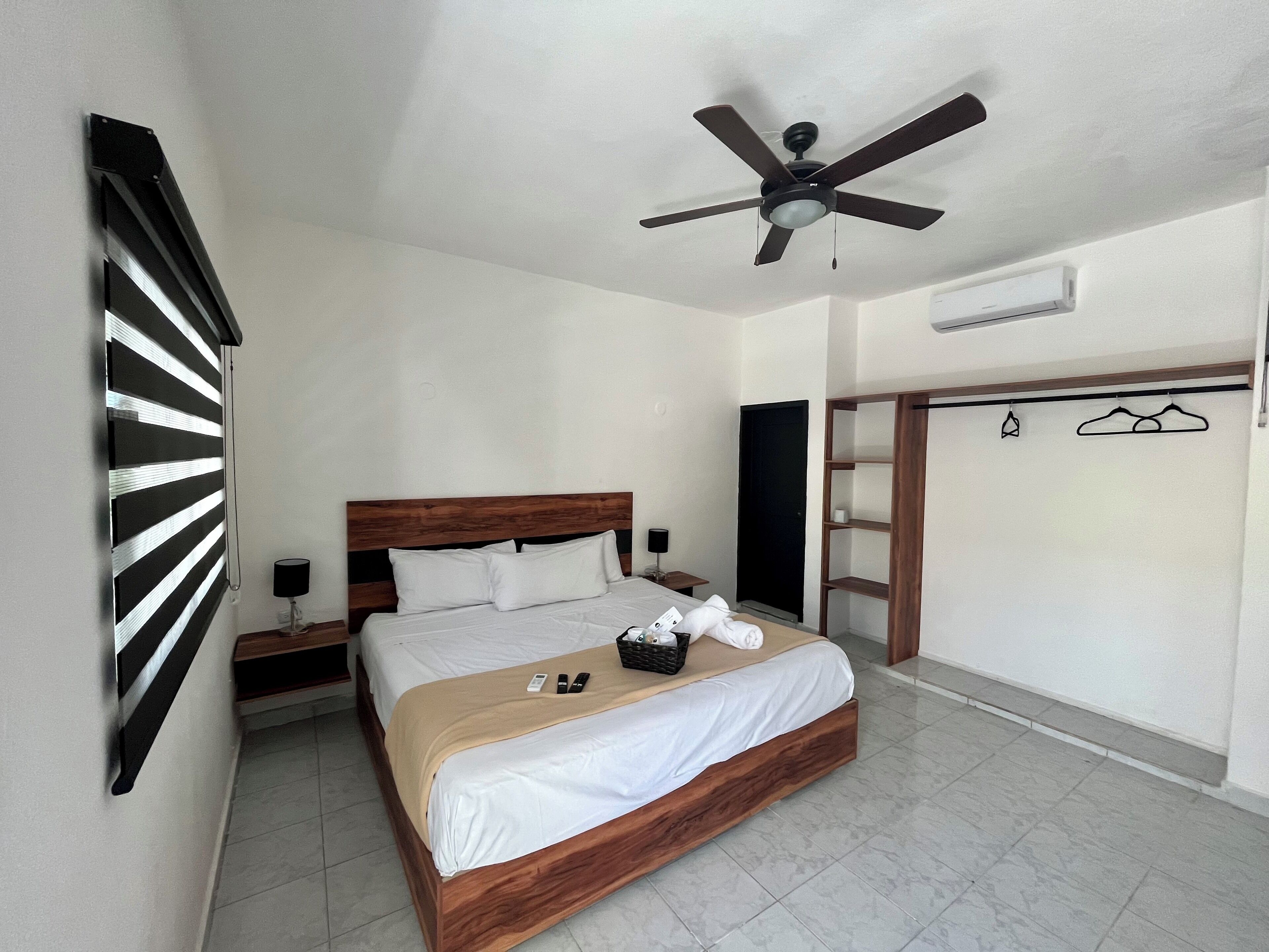 Une chambre d’hôtel équipée d’un lit, d’un ventilateur de plafond, d’une armoire et d’une fenêtre avec des stores.