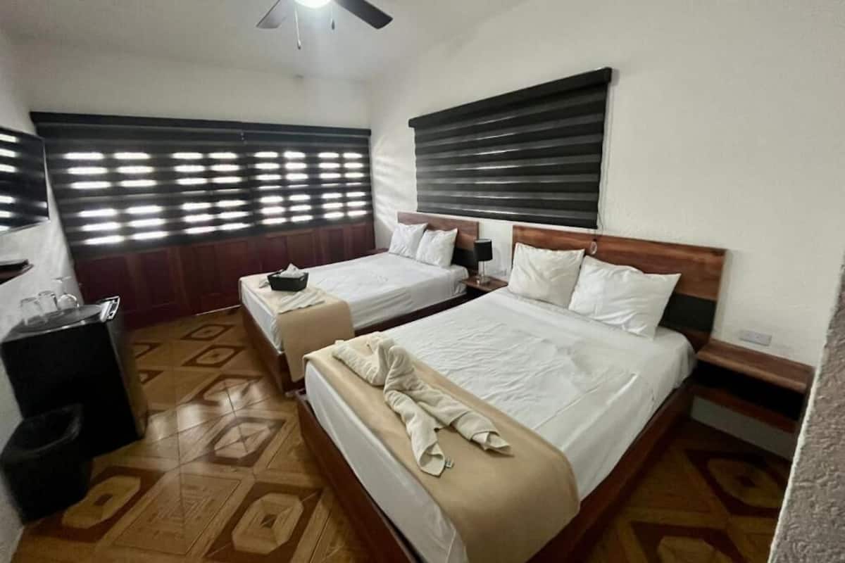 Quarto de hotel com duas camas, um ventilador de teto e uma janela com persianas.