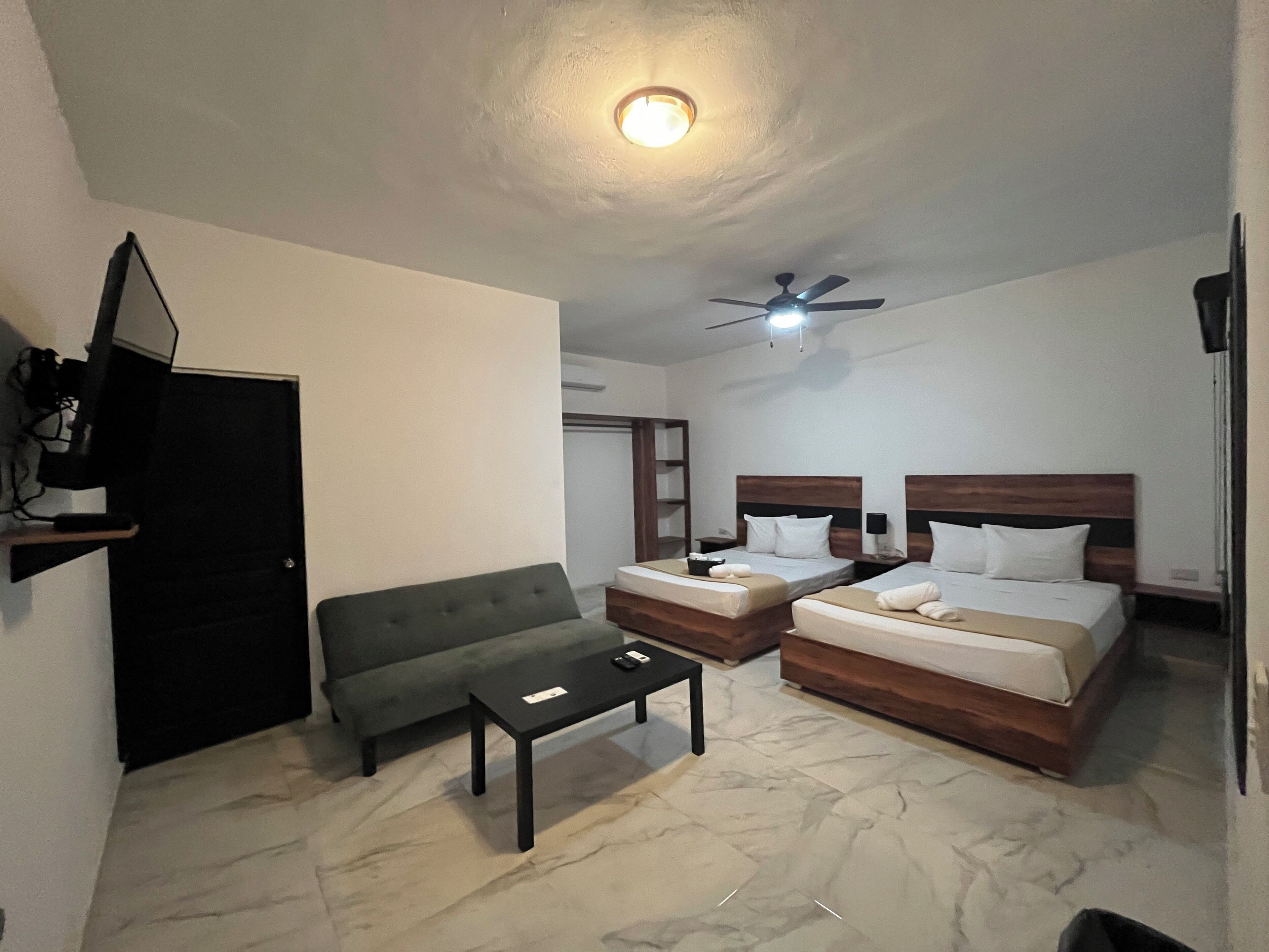 A hotel room with two beds, a sofa, a coffee table, a ceiling fan, and a TV.