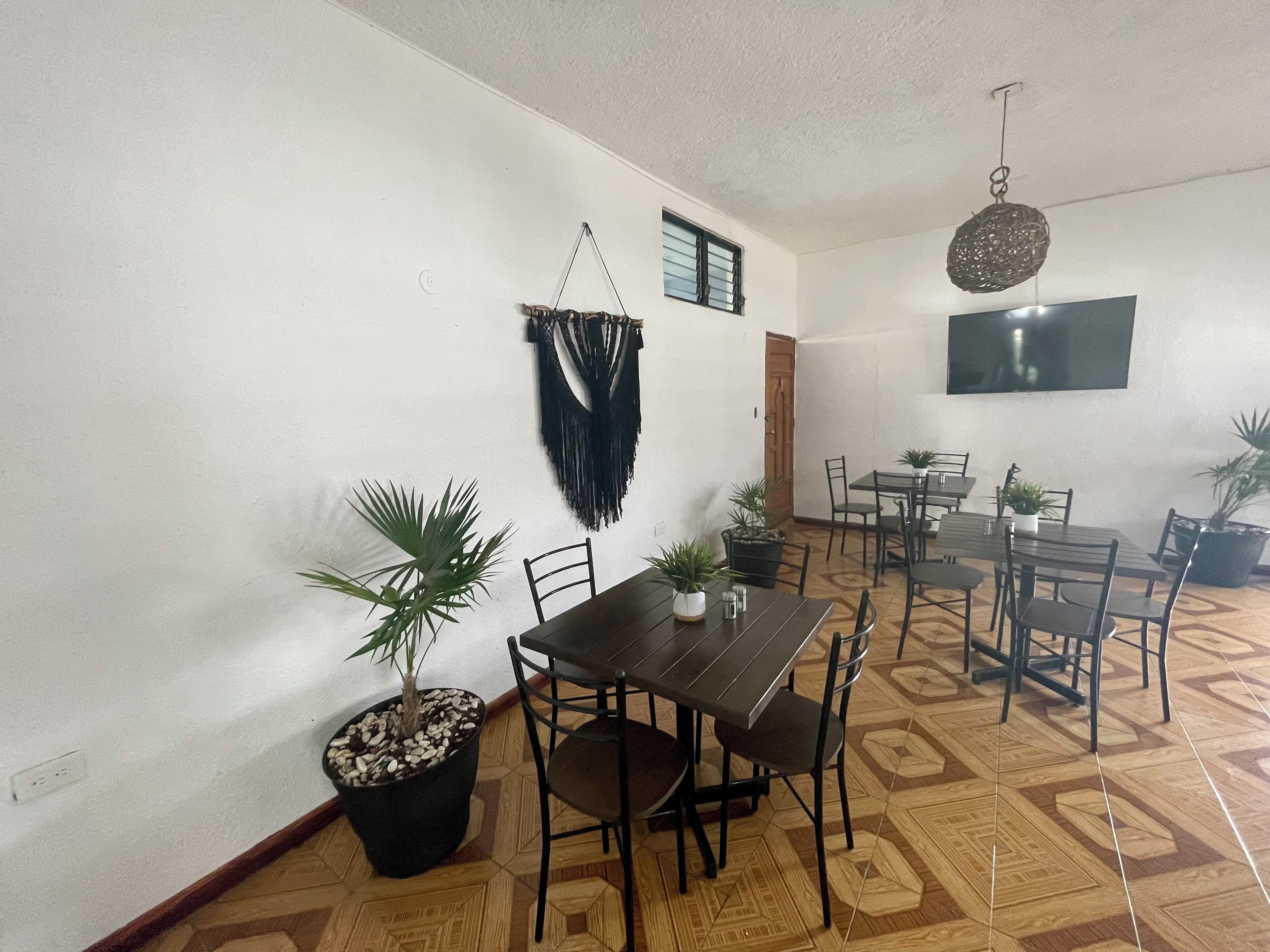 A dining area with a wooden table and chairs, potted plants, and a wall-mounted TV.