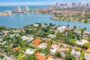 An aerial view of a coastal residential area with multiple buildings, a marina with boats, and a clear view of the ocean.