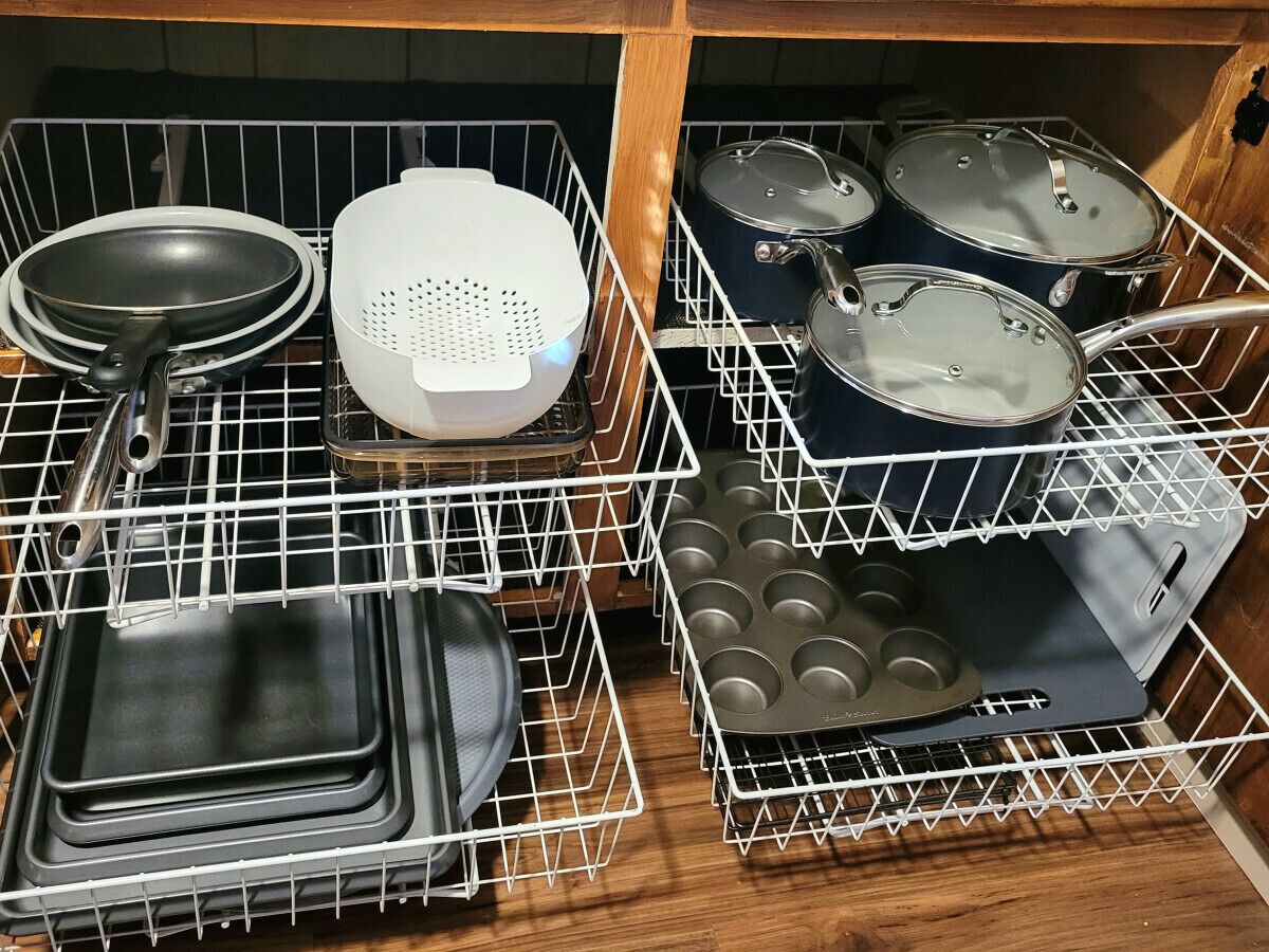 A kitchen with white wire racks holding various cookware, including frying pans, a colander, pots, and a muffin tray.