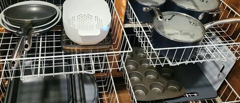 A kitchen with white wire racks holding various cookware, including frying pans, a colander, pots, and a muffin tray.
