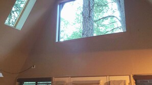 Une pièce dotée d’une lucarne, d’une fenêtre donnant sur un arbre et d’un lit avec une tête de lit.