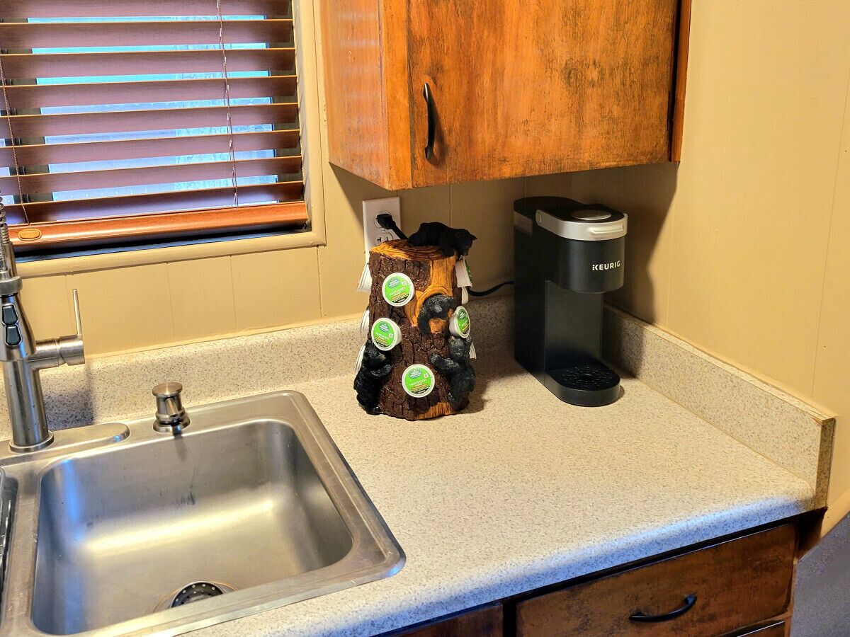 A kitchen with a stainless steel sink, wooden cabinets, a coffee maker, and a decorative tree trunk with green labels.
