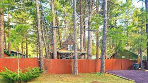 Un quartier résidentiel avec une clôture en bois, une petite maison dotée d’un toit végétalisé et de grands pins.