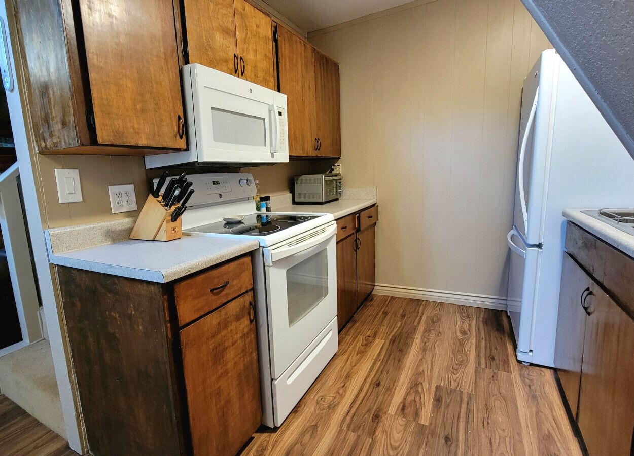A kitchen with wooden cabinets, a white stove, a microwave, and a refrigerator.
