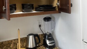 Una cocina con encimera de granito, licuadora, cafetera y un armario con platos y tazones.