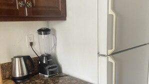 Una cocina con encimera de granito, refrigerador blanco, licuadora, cafetera y armarios de madera.