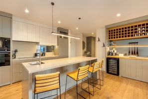 A modern kitchen with a central island, bar stools, a built-in wine rack, and a coffee machine.