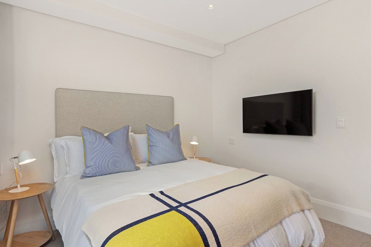 A hotel room with a bed, a television mounted on the wall, and a bedside table with a lamp.