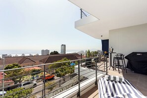 A balcony with a city view, a dining area with a table and chairs, and a covered grill. - Luxury Sea Point Pad with Ocean balcony views (Cape Town)