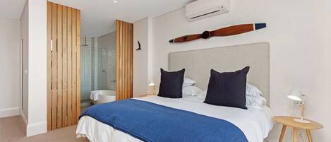 A modern hotel room with a large bed, a wooden partition, an air conditioning unit, and a small bedside table with a lamp.