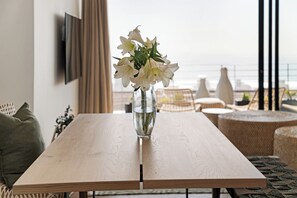 A wooden table with a clear glass vase containing white flowers, positioned in a room with a view of the sea.