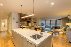 A modern kitchen with a central island, a dining area with yellow chairs, and a large window overlooking a cityscape.