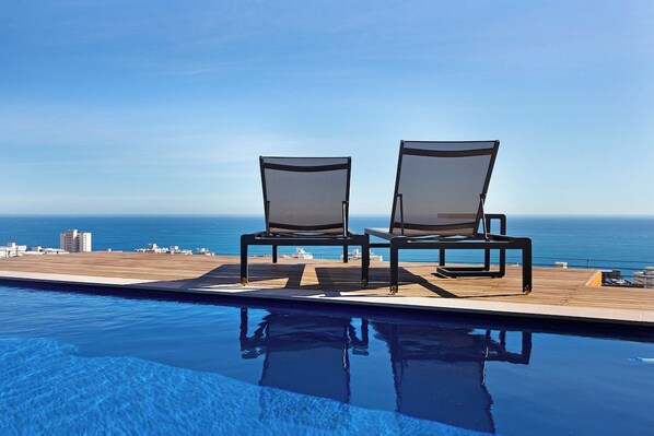 A poolside area with two lounge chairs facing a clear view of the ocean.