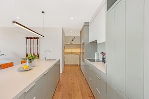 A modern kitchen with a long countertop, wooden flooring, and a hanging light fixture. - Luxury Sea Point Pad with Ocean balcony views (Cape Town)
