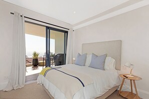 A modern bedroom with a large bed, a bedside table, and a view of the outdoors. - Luxury Sea Point Pad with Ocean balcony views (Cape Town)