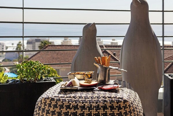A balcony with a woven ottoman, a metal container with snacks, and a small potted plant.