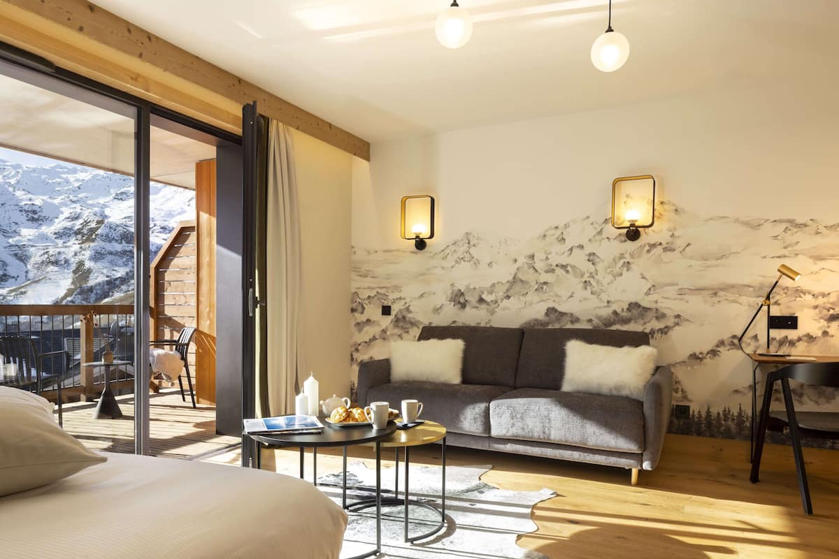 Une pièce chaleureuse avec un canapé, une table basse et une vue sur des montagnes enneigées, visible à travers de grandes fenêtres.