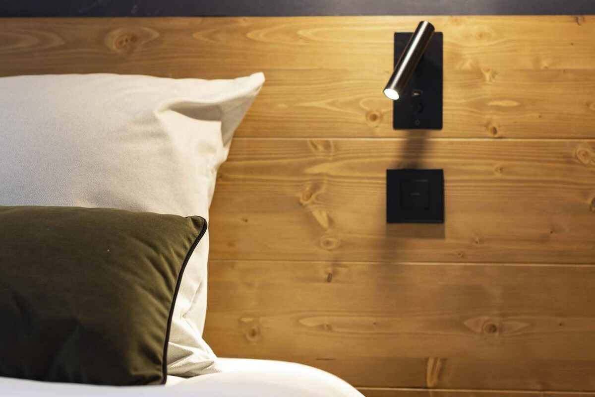 Un dormitorio con cabecera de madera, una lámpara de noche y vistas al exterior.