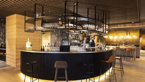 A modern bar area with a circular counter, stools, and a bartender. - Higalik Hotel (Les Belleville)