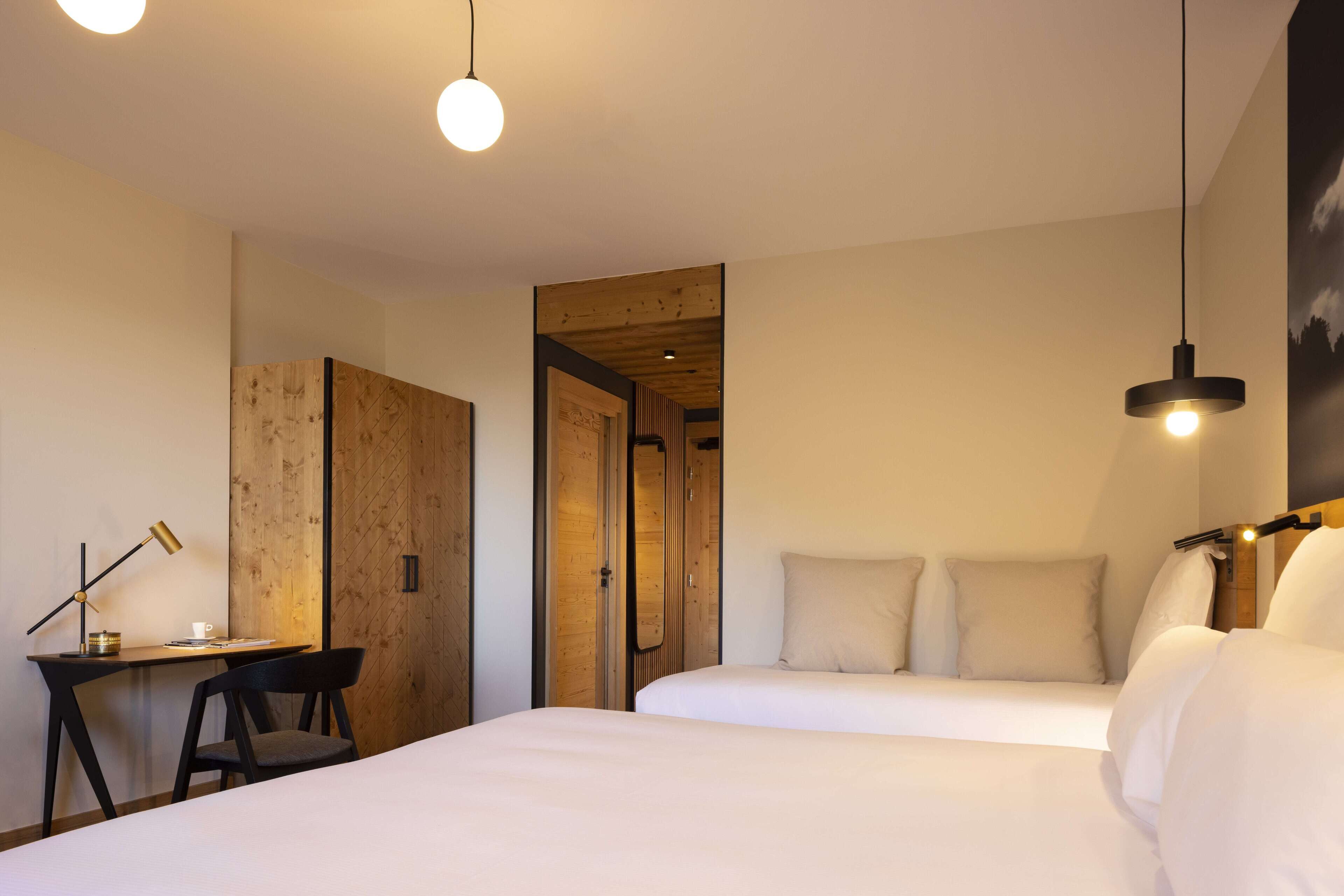 A hotel room with two beds, a desk with a chair, and a wooden wardrobe.