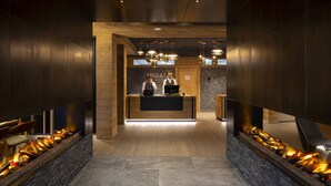 A reception area with a wooden reception desk, two staff members, and a modern fire feature along the walls. - Higalik Hotel (Les Belleville)