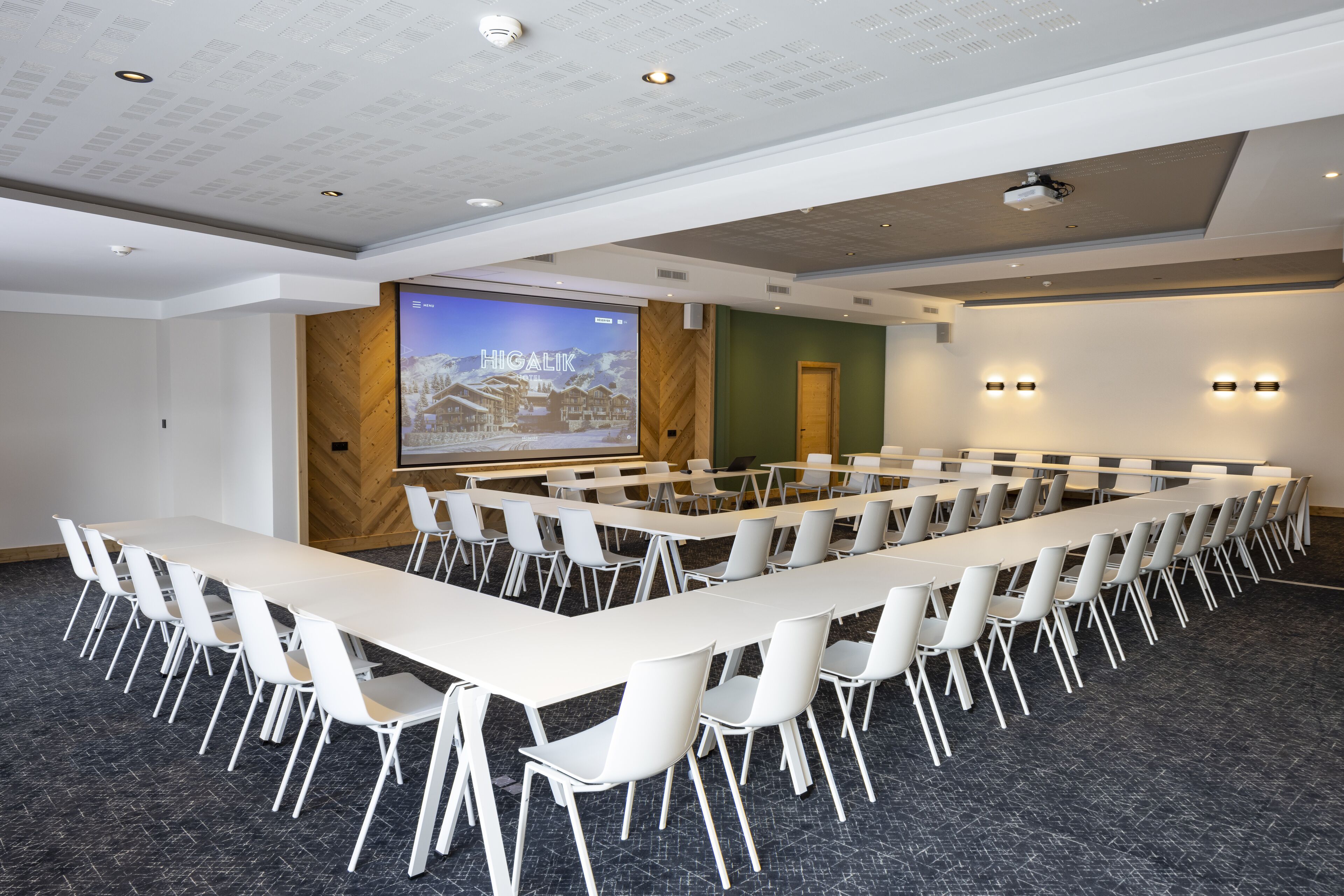 A conference room with a long table, white chairs, a projector screen, and a large screen displaying a snowy village.