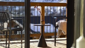A wooden deck with a view of snow-covered mountains. There are two chairs and a small table with a vase of dried flowers. - Higalik Hotel (Les Belleville)