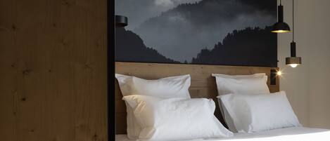 A bedroom with a wooden headboard, white bedding, and a mountain landscape mural on the wall.