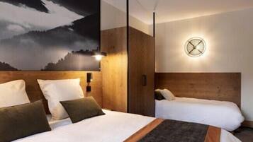 A hotel room with a large bed, a smaller bed, a wall clock, and a mountain landscape painting.