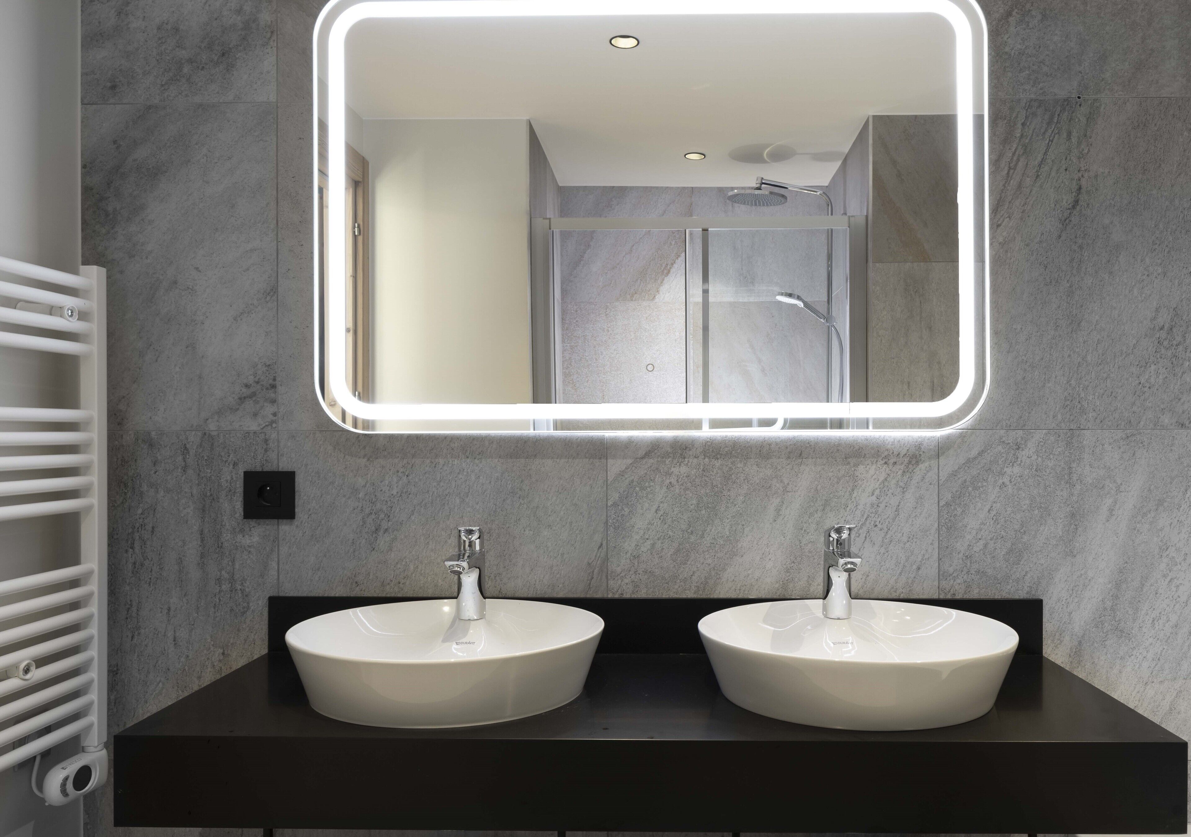 Un baño moderno con dos lavamanos blancos, un espejo grande con iluminación LED y una zona de ducha.