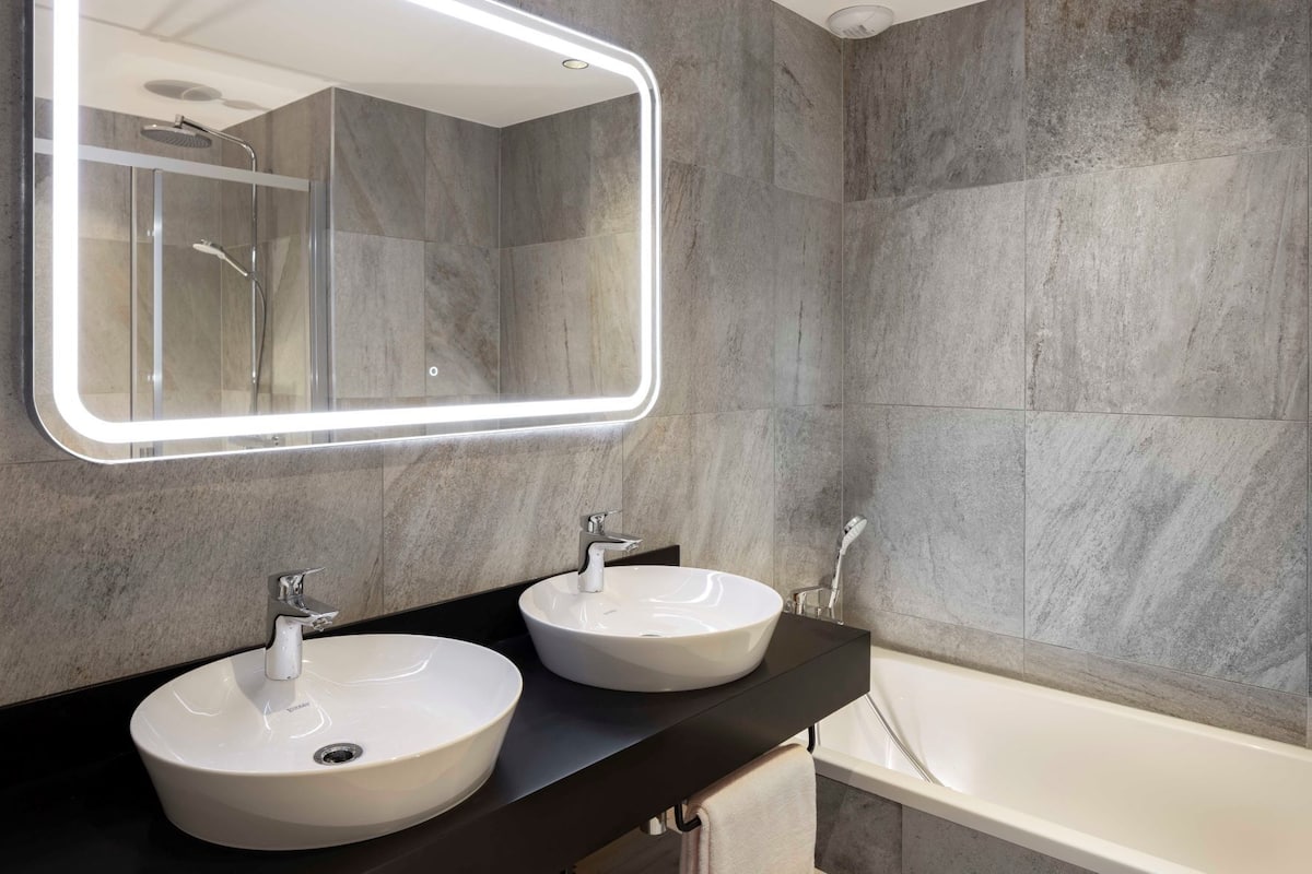 Une salle de bain moderne avec deux vasques rondes, un grand miroir et une baignoire.