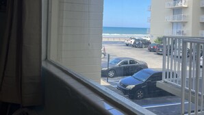Vista desde una ventana sobre un estacionamiento con varios coches, un edificio con balcones y un cielo azul despejado.