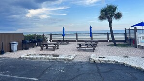 Un patio frente a la playa con mesas de picnic y sombrillas, con vista al océano.