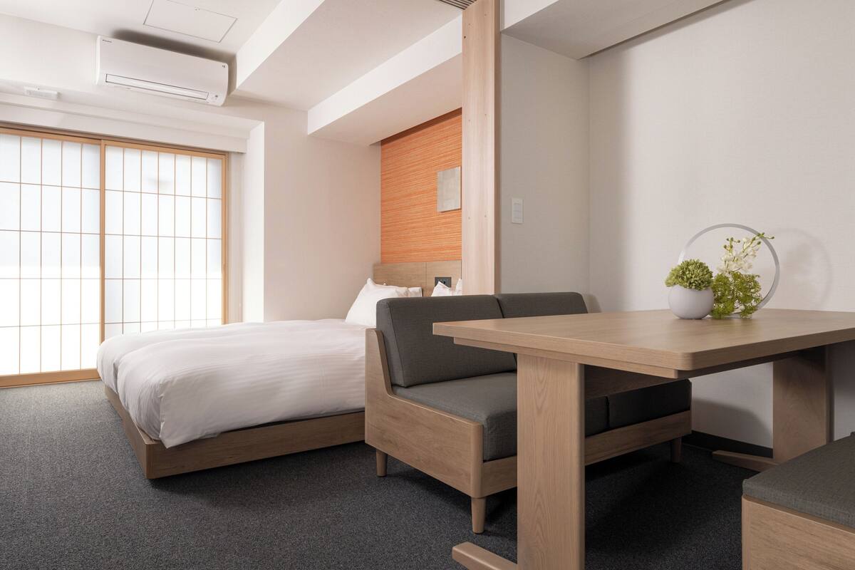 Una habitación de hotel moderna con cama, sofá, una mesita y una planta en maceta.