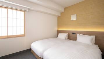 A hotel room with a large bed, a window with blinds, a wooden headboard, and a wall-mounted light fixture.
