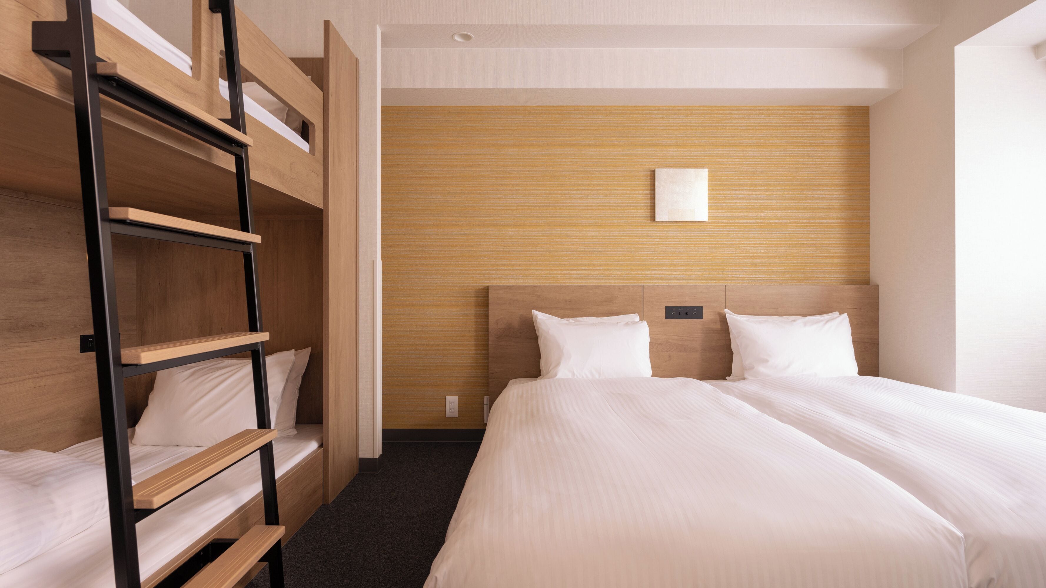 Une chambre d’hôtel avec un lit superposé, un lit simple et une tête de lit en bois.
