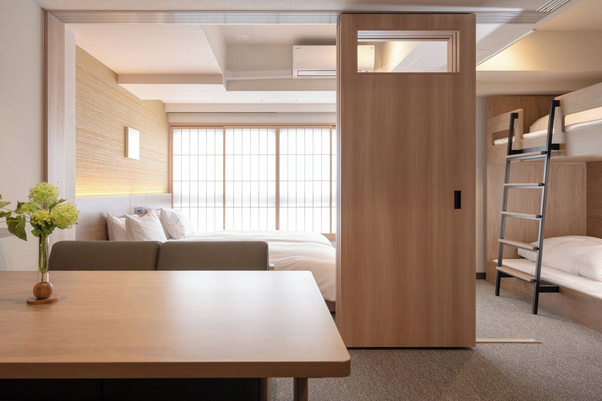 Una habitación de hotel moderna con una mesa de madera, un sofá, una litera y una ventana con persianas.