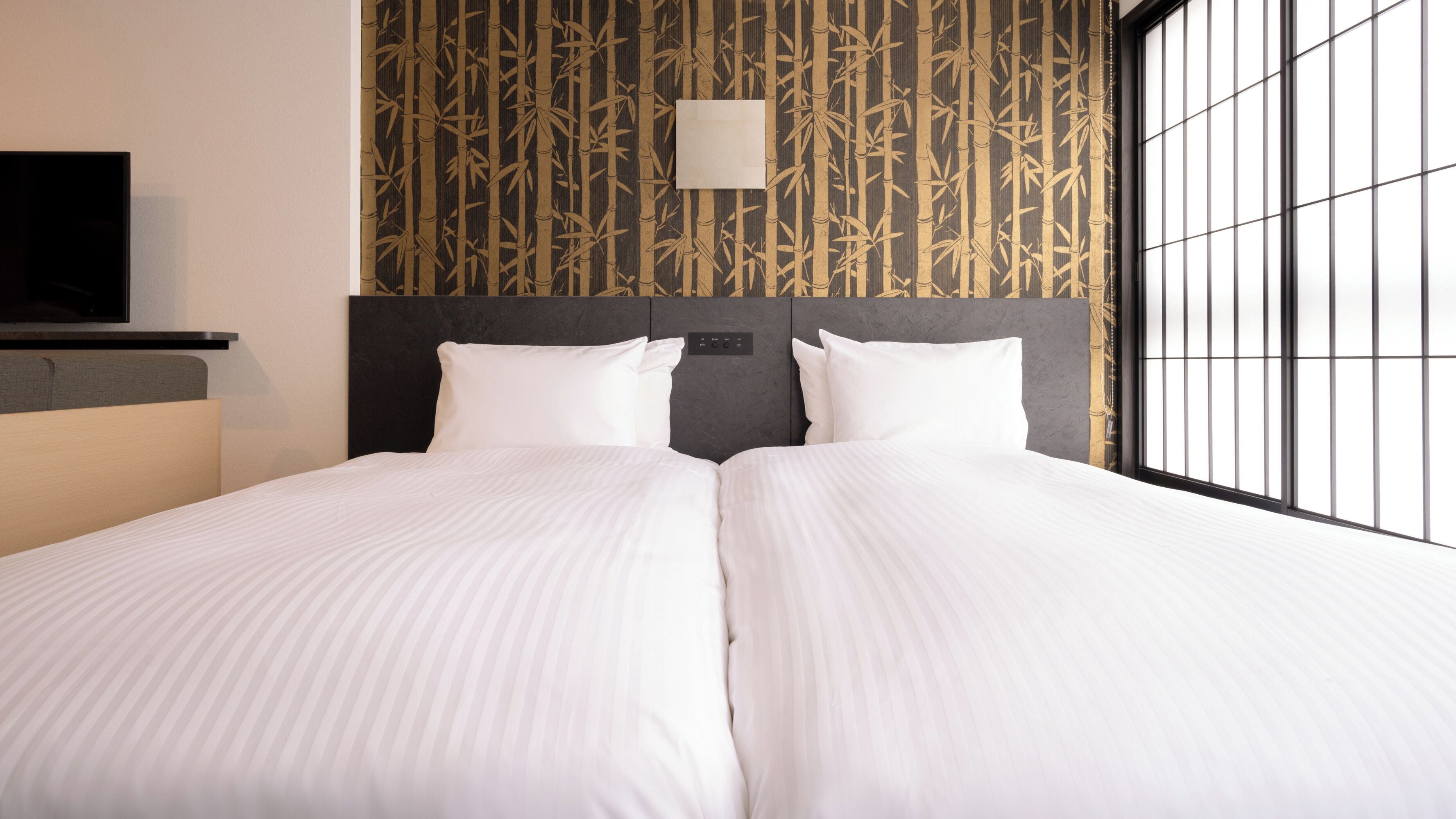 A double bed with white linens, a headboard with a control panel, and a wall with a bamboo pattern.