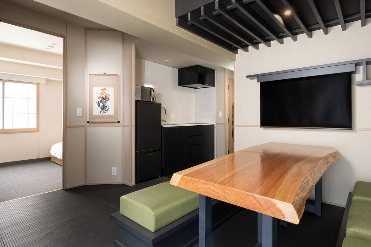 Cocina compacta con estufa integrada, refrigerador negro y una mesa de comedor de madera con bancos acolchados verdes.