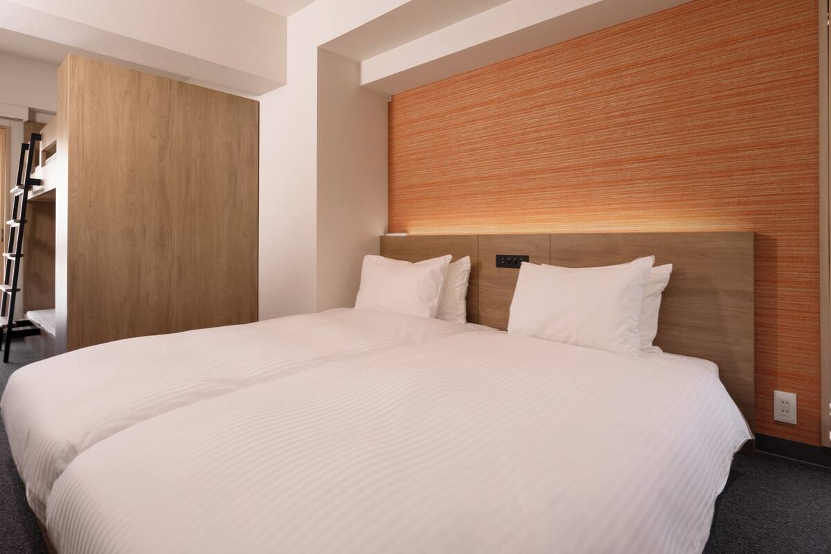 Una cama grande con cabecera de madera y dos almohadas, un armario de madera y una ventana con persianas.