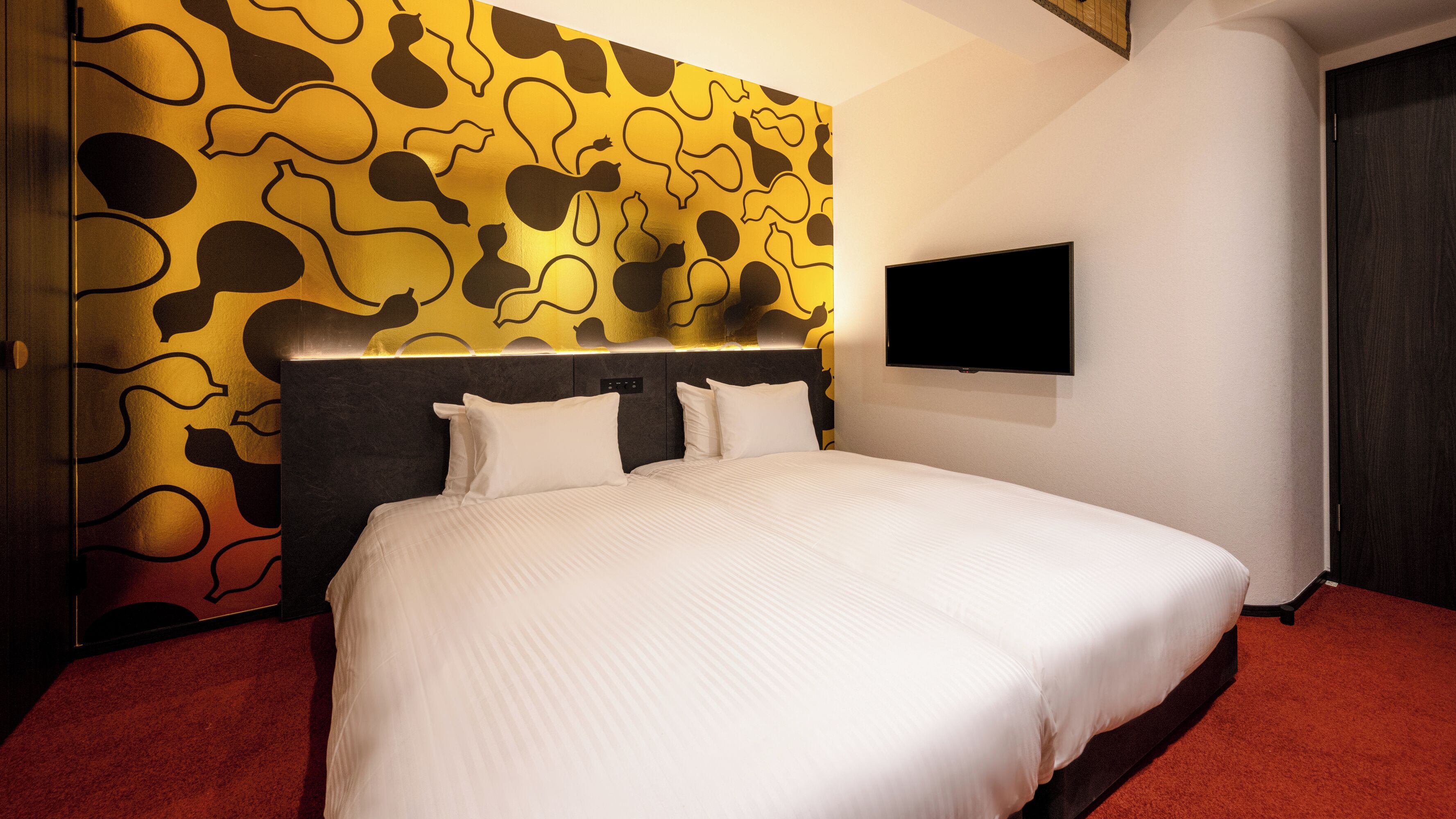 A hotel room with a bed, a television on the wall, and a patterned wall.