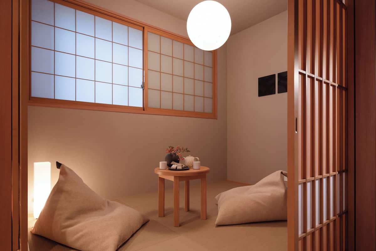 A traditional Japanese room with tatami flooring, a shoji screen, a small wooden table with tea set, and two cushions.