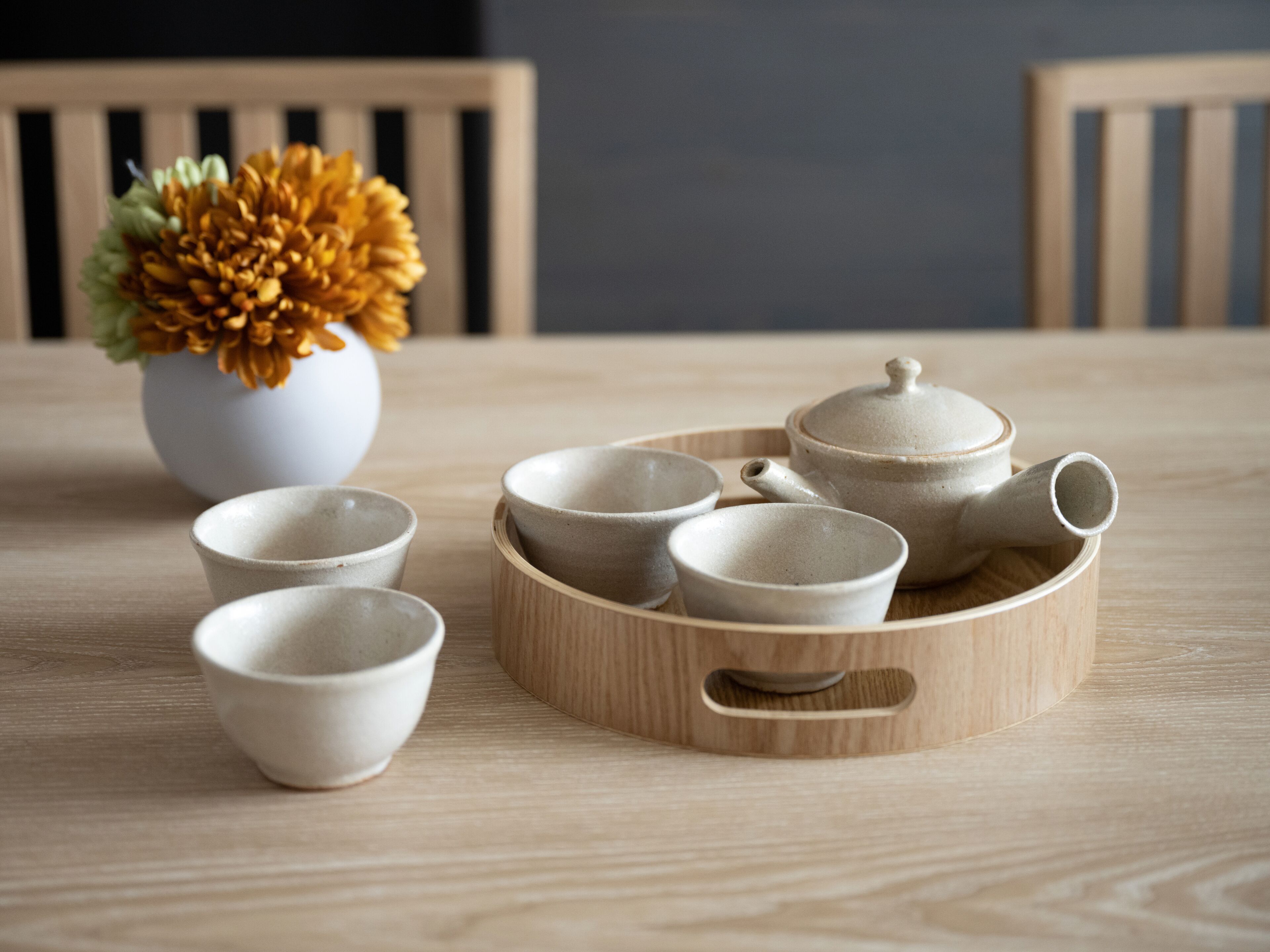A wooden table with a set of ceramic tea cups and a teapot on a tray.