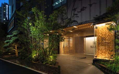 A modern building with a wooden facade, a sign for the MIMARU APARTMENT HOTEL, and a well-lit entrance area with plants.