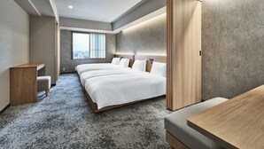 A modern hotel room with a large bed, a desk, and a view of the city through a large window.