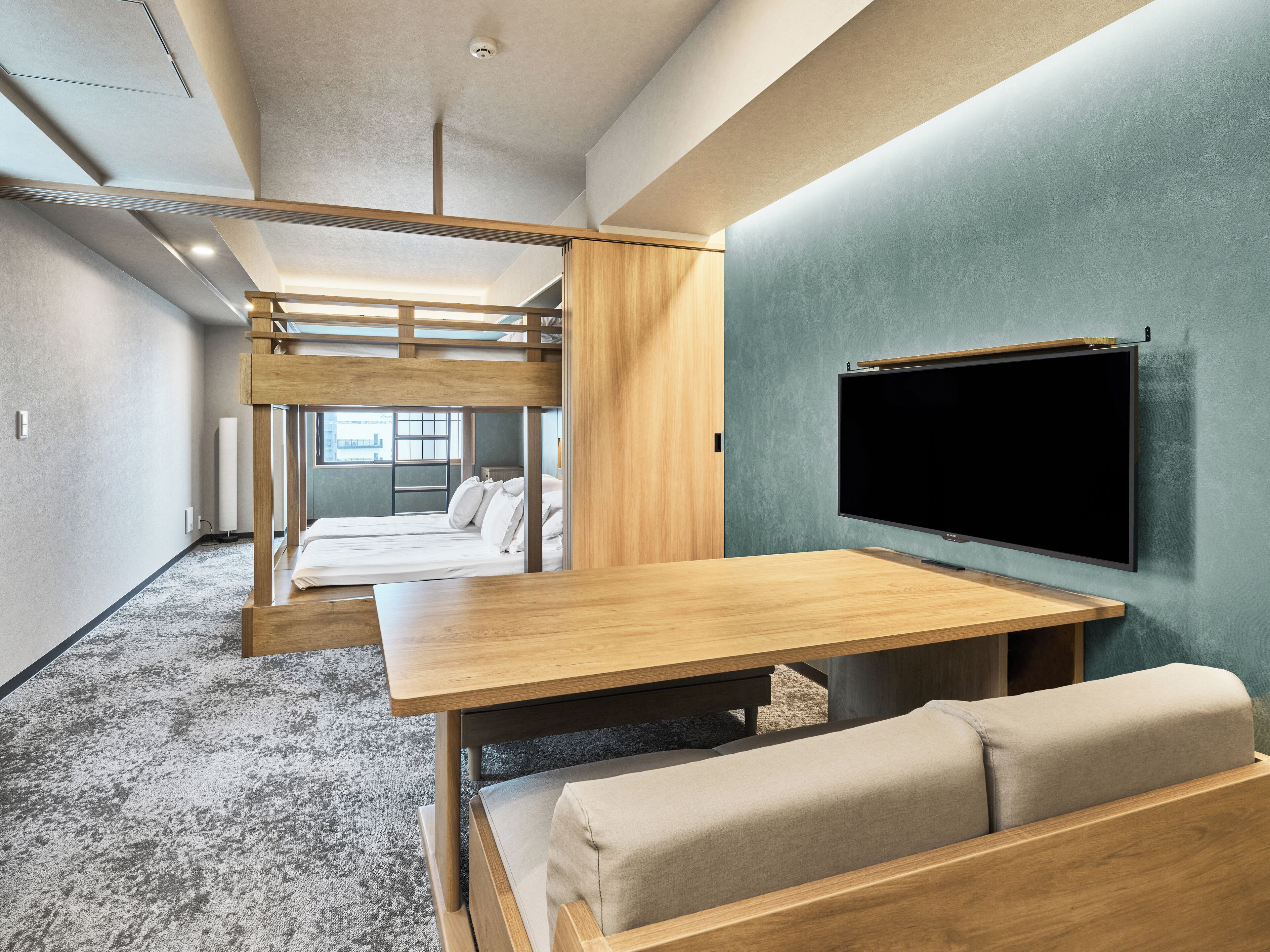 A bunk bed with a wooden frame, a flat-screen TV mounted on the wall, and a wooden table with a bench.